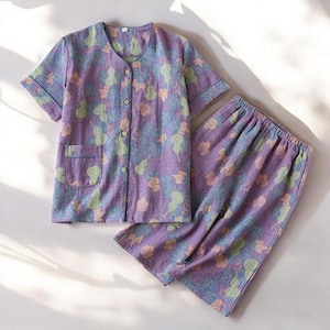 Puede incluir: Un conjunto de pijama de estampado floral morado y verde con una parte superior de manga corta con botones y pantalones largos.