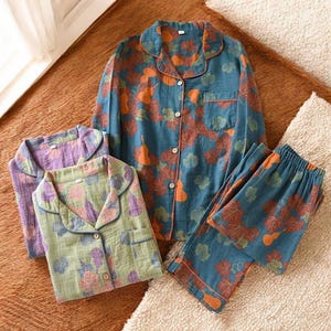 Puede incluir: Tres conjuntos de pijamas con fondo azul, verde y morado. Cada conjunto presenta un estampado de hojas y calabazas en naranja y marrón.