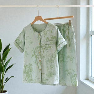 Può includere: Un completo pigiama verde chiaro con stampa a bambù. La maglia a maniche corte ha una chiusura con bottoni e una tasca sul petto. I pantaloni abbinati hanno un elastico in vita. Il set è appeso a una gruccia di legno.