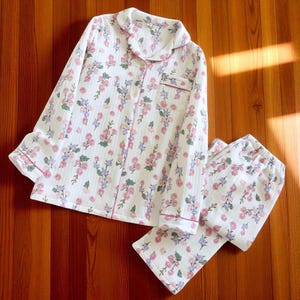 Peut inclure: Ensemble de pyjama blanc avec un motif floral de fleurs roses et violettes. Le haut à manches longues a une fermeture boutonnée, une poche poitrine et une bordure rose. Le pantalon assorti a une taille élastique.