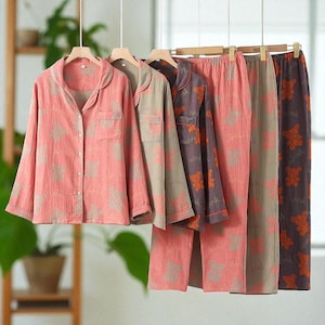 May include: A collection of pajama sets in various colors, including pink, tan, and purple. Each set features a button-down shirt and matching pants, all adorned with a repeating bear pattern. The pajamas are hanging on wooden hangers.