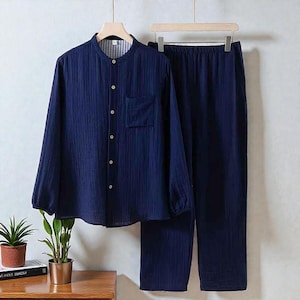 Puede incluir: Conjunto de pijama azul marino. La camisa de manga larga tiene cuello mao, bolsillo en el pecho y botones. Los pantalones a juego tienen cintura elástica. El conjunto está hecho de tela texturizada y se muestra en una percha.