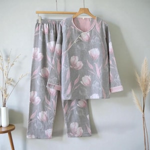 Op de afbeelding: Grijze pyjamaset met een bloemenpatroon van roze tulpen en groene bladeren. De top met lange mouwen heeft een wikkel sluiting met een roze binnenkant en witte bies. De bijpassende broek heeft een elastische tailleband.