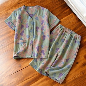May include: A green and purple floral print pyjama set with short sleeves and trousers. The top has a button fastening and a pocket on the left side.