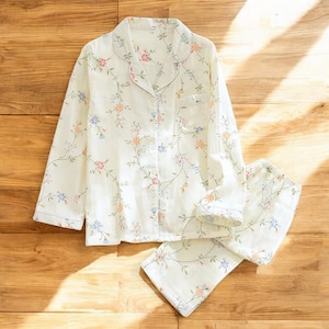 May include: A white pyjama set with a floral print. The top has a button-up front and long sleeves. The trousers are long and have a straight leg.