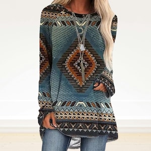 Op de afbeelding: Een tuniek met lange mouwen met een geometrisch patroon in tinten blauw, bruin en beige. De tuniek heeft een ronde hals en een losse pasvorm. Het ontwerp heeft ruit- en zigzagpatronen. De mouwen hebben een uitlopende manchet.