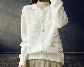 May include: Cream-colored cardigan sweater with a textured knit design. The sweater features floral embroidery with pearl accents and decorative buttons. A stylish and elegant piece for layering.