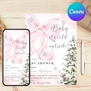 May include: A baby shower invitation and a phone screen displaying the same design. The design features a pink bow with pearl accents, snowflakes, and the text "Baby it's cold outside!". A pen rests on a wooden surface.