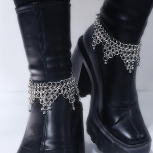 May include: Black leather platform boots with silver chain anklets. The boots have a chunky heel and a rounded toe. The chain anklets are made of small, interconnected rings and dangle with small silver beads.