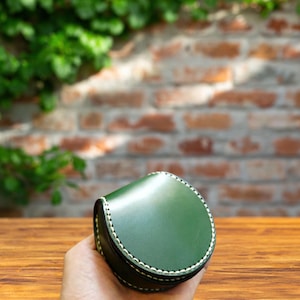 May include: A green leather coin purse with a white stitch detail. The purse is closed and has a rounded shape.
