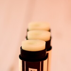May include: Four lip balm tubes with black and white striped labels. The lip balm is a light yellow color.