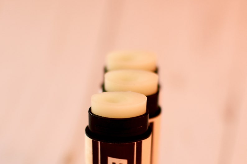 May include: Four lip balm tubes with black and white striped labels. The lip balm is a light yellow color.