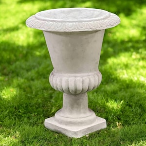 May include: A light gray, ornate garden urn with a wide, decorative rim and a pedestal base. The urn is made of a stone-like material and sits on a square base. The background is green grass.