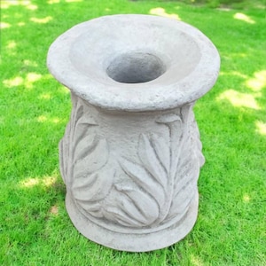 May include: A gray concrete pedestal with a decorative leaf design. The pedestal has a round top and a wide base.