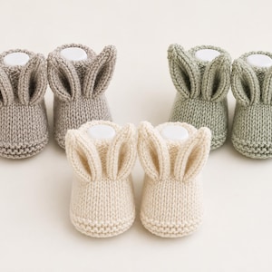 Puede incluir: Tres pares de patucos de punto para bebé en beige, verde salvia y crema. Cada par presenta dos orejas de conejo puntiagudas y erguidas en la parte superior. Los patucos tienen un borde de punto bobo texturizado en la base y un cuerpo de punto liso.