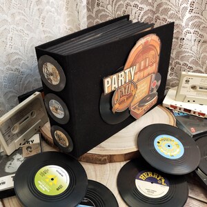 Puede incluir: Un álbum negro con un diseño retro "Party Jazz" y varios discos de vinilo. El álbum tiene discos de vinilo decorativos adheridos al lateral. Otros discos de vinilo y cintas de cassette están esparcidos alrededor del álbum.