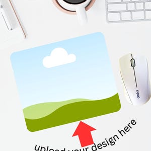 Puede incluir: Un ratón blanco con un diseño de cielo azul y hierba verde. El texto "upload your design here" está escrito debajo del ratón con una flecha roja apuntando hacia arriba.