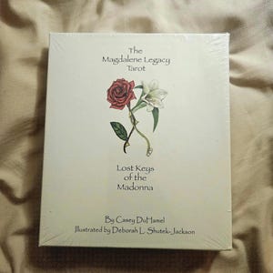 May include: A sealed tarot card deck titled "The Magdalene Legacy Tarot." The cover features a red rose and a white lily illustration. The text "Lost Keys of the Madonna" and author and illustrator names are also visible.