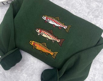 May include: Dark green sweatshirt featuring embroidered fish in shades of red, yellow, and brown. The sweatshirt has a crew neck and long sleeves with ribbed cuffs. The fish are arranged in a vertical pattern.