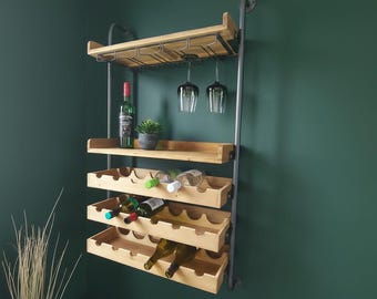 May include: A wooden wine rack with a metal frame, holding wine bottles, wine glasses, and a small potted plant. The rack has multiple shelves for bottle storage and a top rack for hanging glasses. The rack is mounted on a dark green wall.