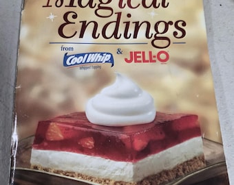 Op de afbeelding: Een magazine cover met de titel "Magical Endings" met een dessert met een witte slagroom topping, een rode gelei laag met fruit en een crème laag op een koekjesbodem. Het magazine is van Cool Whip en Jell-O.
