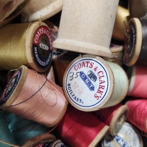 May include: A close-up of a pile of wooden spools of thread. The spools are in various colors, including red, pink, blue, green, and yellow. The spools are labeled with the brand name "Coats & Clark's" and the text "O.N.T."