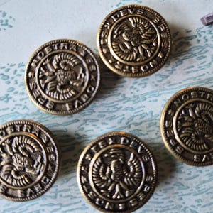 May include: Five round, metallic, bronze-toned buttons featuring a raised relief design of an eagle with wings spread. The border of each button is inscribed with the Latin text SPES NOSTRA DEUS EST, arranged in a circular pattern around the central eagle.