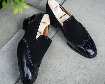 May include: A pair of black leather slip-on shoes with a brogue design and a patent leather toe. The shoes have a decorative pattern of small holes.