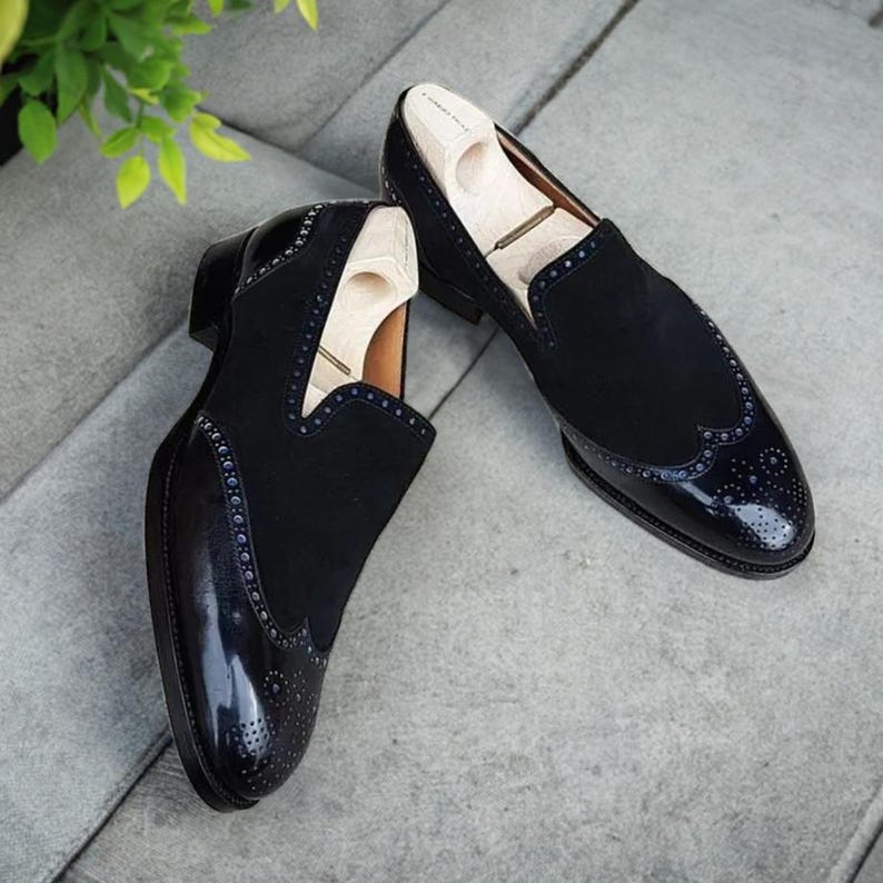 May include: A pair of black leather slip-on shoes with a brogue design and a patent leather toe. The shoes have a decorative pattern of small holes.