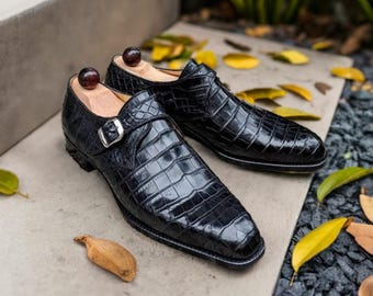 May include: A pair of black leather dress shoes with a crocodile pattern. The shoes have a buckle strap and a pointed toe.