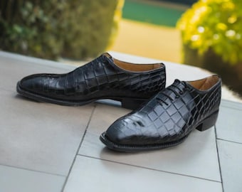 May include: A pair of black leather lace-up shoes with a crocodile pattern. The shoes are on a tiled surface.