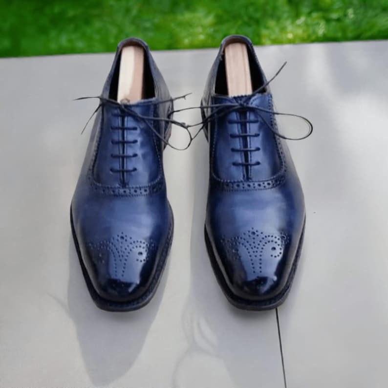 May include: A pair of dark blue leather oxford shoes with brogue detailing and lace-up closures.