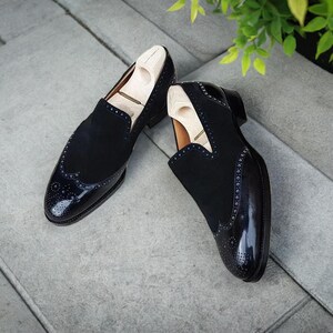 May include: A pair of black leather slip-on shoes with a wingtip design and a suede upper. The shoes have a black patent leather toe cap and a brogue pattern.