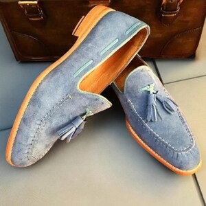 May include: A pair of blue suede tassel loafers with light blue stitching and a brown leather sole.