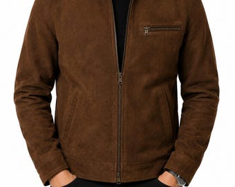 May include: A brown suede jacket featuring a classic collar, a full-length front zip, long sleeves with cuffs, and a single horizontal zipped chest pocket on the left side. The jacket is worn over a black shirt and black trousers.