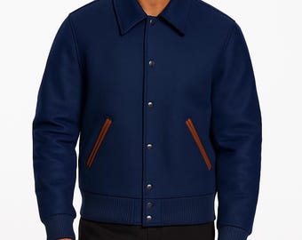 May include: A navy blue jacket featuring a classic collar, long sleeves with ribbed cuffs, and a ribbed hem. The front closure consists of five silver-toned snap buttons. Two slanted welt pockets with brown leather-like trim are positioned on the front.