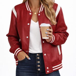 Pode incluir: Casaco bomber vermelho com riscas brancas nas mangas e gola. O casaco tem detalhes brancos nos ombros e punhos. Apresenta um fecho de botões e é combinado com jeans azul escuro.