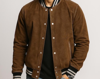May include: A brown suede varsity jacket featuring a ribbed collar and cuffs with white and black stripes. The jacket has a front button closure with silver-toned metal snaps, long sleeves, and a solid brown finish. It is worn over a black shirt.
