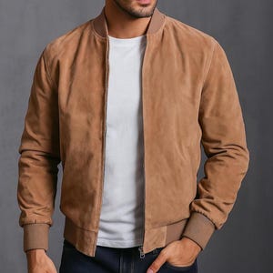 May include: A tan suede bomber jacket with a ribbed collar, cuffs, and hem. The jacket features a front zip and is worn over a white t-shirt. The jacket's neutral tone makes it versatile for different outfits.