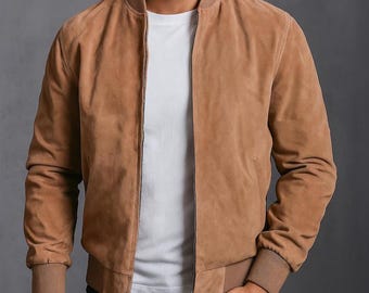 May include: A tan suede bomber jacket featuring a ribbed collar, cuffs, and hem. The jacket is worn open over a plain white t-shirt. It has a central metal zip closure and long sleeves, providing a clean, structured look with a soft texture.