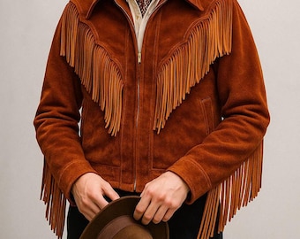 May include: A brown suede jacket with long fringe detailing across the chest and sleeves. The jacket has a zipper closure and a collar. A brown fedora hat is held in the hands. The person is wearing a patterned scarf and a white shirt.