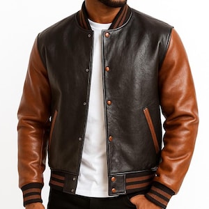 Könnte beinhalten: Eine schwarze und braune Leder-Collegejacke mit braunen Ärmeln, geripptem Kragen, Bündchen und Saum. Die Jacke hat eine Knopfleiste und zwei Vordertaschen. Getragen über einem weißen T-Shirt.