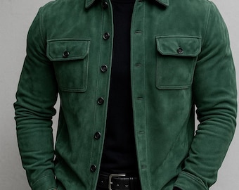 May include: A forest green button-down shirt jacket with a soft, matte texture, featuring a classic collar, long sleeves, and two chest pockets with buttoned flaps. The garment is worn over a black mock neck shirt and black trousers with a black belt.