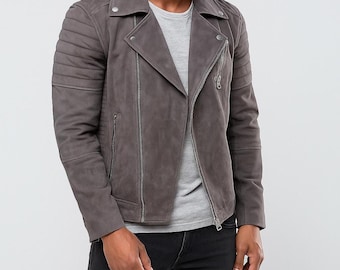 Può includere: Giacca da motociclista in camoscio grigio con colletto a revers, chiusura asimmetrica con zip e dettagli trapuntati sulle spalle. La giacca ha più tasche con zip e un risvolto con bottoni a pressione. Il modello indossa una maglietta grigia e jeans neri.