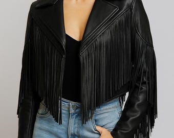 Puede incluir: Una chaqueta negra corta con largos flecos en los paneles delanteros y en las mangas. La chaqueta presenta un cuello de solapa ancho, mangas largas y un acabado liso. Se lleva sobre una camiseta negra y unos vaqueros azul claro.