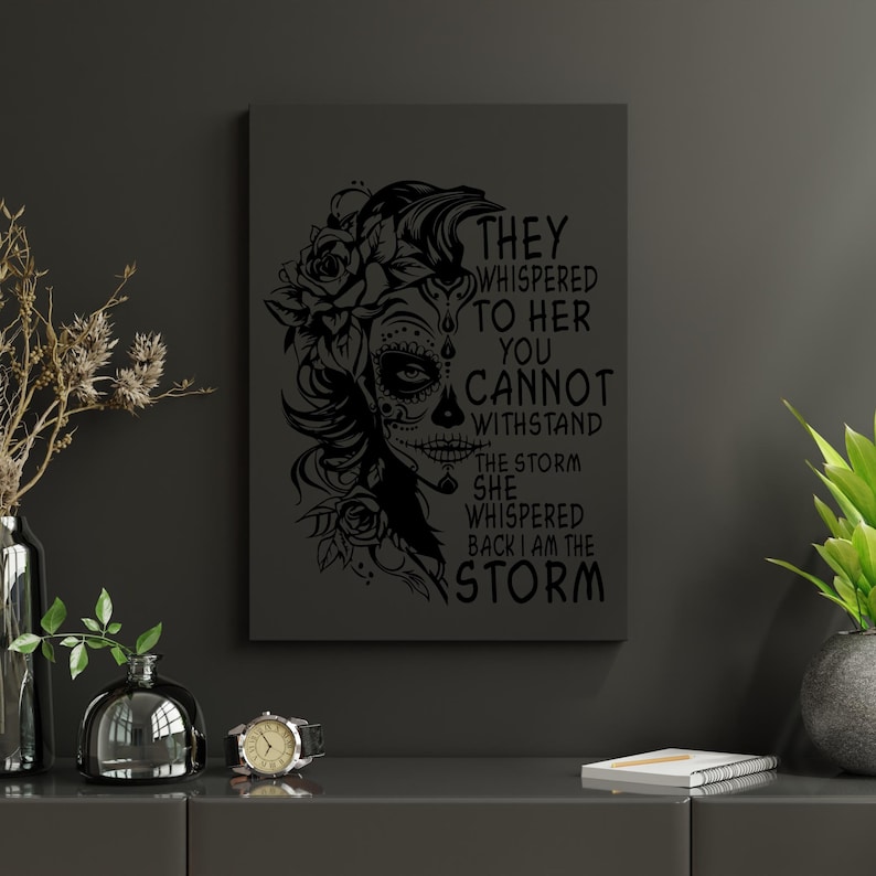 May include: Black and white illustration of a woman with a sugar skull face and flowers. The text reads "They whispered to her you cannot withstand the storm she whispered back I am the storm."