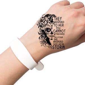 May include: Black and white temporary tattoo with a sugar skull design and the text "They whispered to her you cannot withstand the storm she whispered back I am the storm".