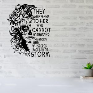 May include: Black and white graphic design featuring a woman with a sugar skull face and floral accents. The text reads "They whispered to her you cannot withstand the storm she whispered back I am the storm."