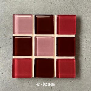 May include: A square mosaic tile sheet with nine glass tiles in shades of red and pink, including a deep burgundy. The tiles are arranged in a 3x3 grid, with a white grout. The text "42 - Blossom" is at the bottom.