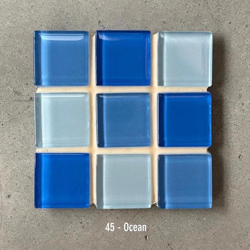 May include: A square mosaic tile sheet with nine glass tiles in shades of blue. The tiles are arranged in a 3x3 grid, with varying hues from light to dark blue. The text "45 - Ocean" is at the bottom.